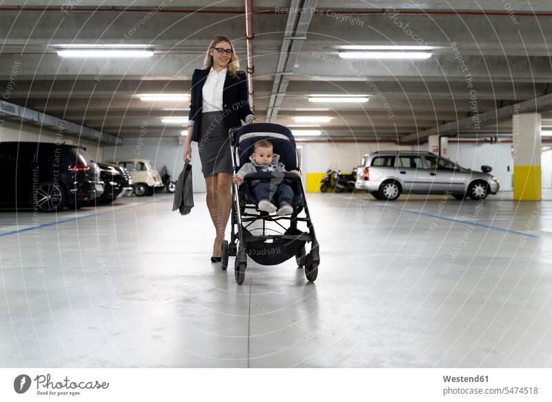 Young businesswoman pushing stroller with baby boy in car park caucasian caucasian ethnicity caucasian appearance european family with one child lifestyle
