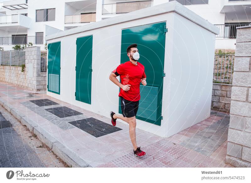 Mid adult man wearing face mask while running on footpath in city color image colour image Spain outdoors location shots outdoor shot outdoor shots day
