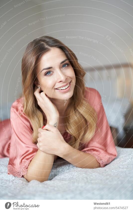 Portrait of smiling young woman in dressing gown lying in bed beds portrait portraits bathrobe females women smile Adults grown-ups grownups adult people