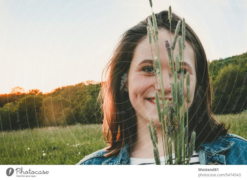 Portrait of smiling teenage girl with grasses at sunset smile hide in the evening summer time summertime summery delight enjoyment Pleasant pleasure pleased