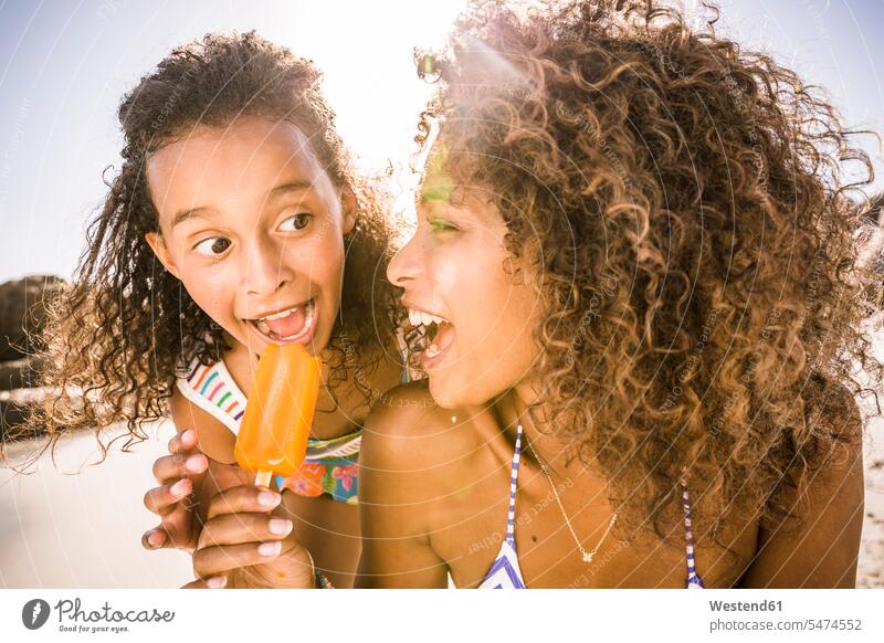 Woman sharing popsicle with daughter on the beach human human being human beings humans person persons curl curled curls curly hair swim wear bikinis give hold