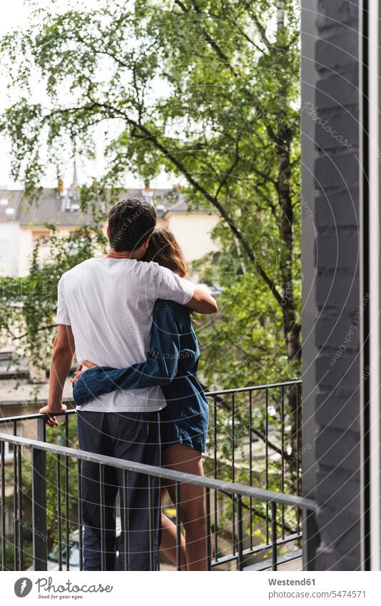 Rear view of couple in nightwear standing on balcony hugging Nightwear balconies twosomes partnership couples home at home embracing embrace Embracement people
