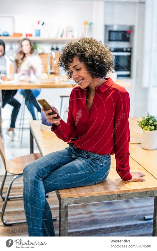 Smiling woman with cell phone sitting on table Seated smiling smile mobile phone mobiles mobile phones Cellphone cell phones females women Table Tables