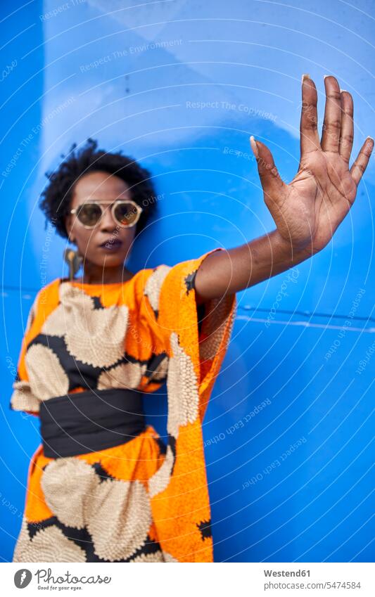 Woman raising her hand in front of blue background dresses Eye Glasses Eyeglasses specs spectacles Pair Of Sunglasses sun glasses stand fashionable stopping