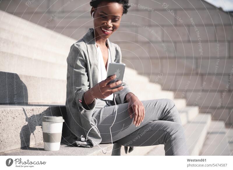 Portrait of smiling businesswoman sitting on stairs using earphones and smartphone Smartphone iPhone Smartphones stairway ear phone ear phones businesswomen
