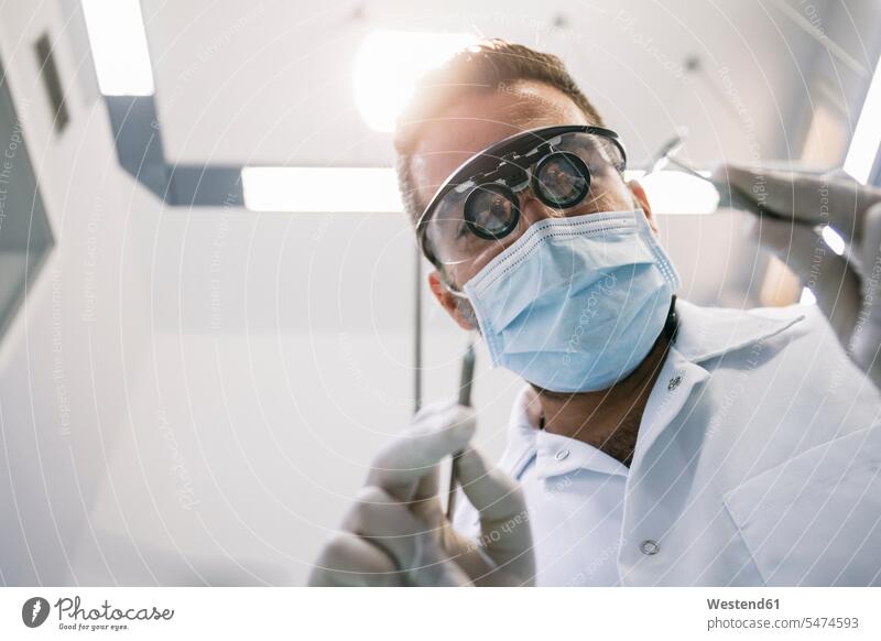 Male dentist in surgical loupes and mask with medical instruments during treatment in clinic color image colour image indoors indoor shot indoor shots interior