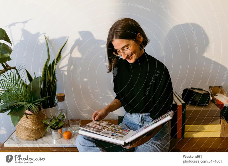 Smiling woman looking photographs in photo album while sitting at home color image colour image indoors indoor shot indoor shots interior interior view
