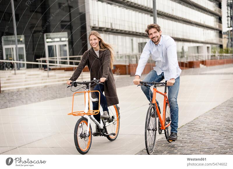 Smiling couple riding bicycle in the city bikes bicycles riding bike bike riding cycling bicycling pedaling twosomes partnership couples town cities towns