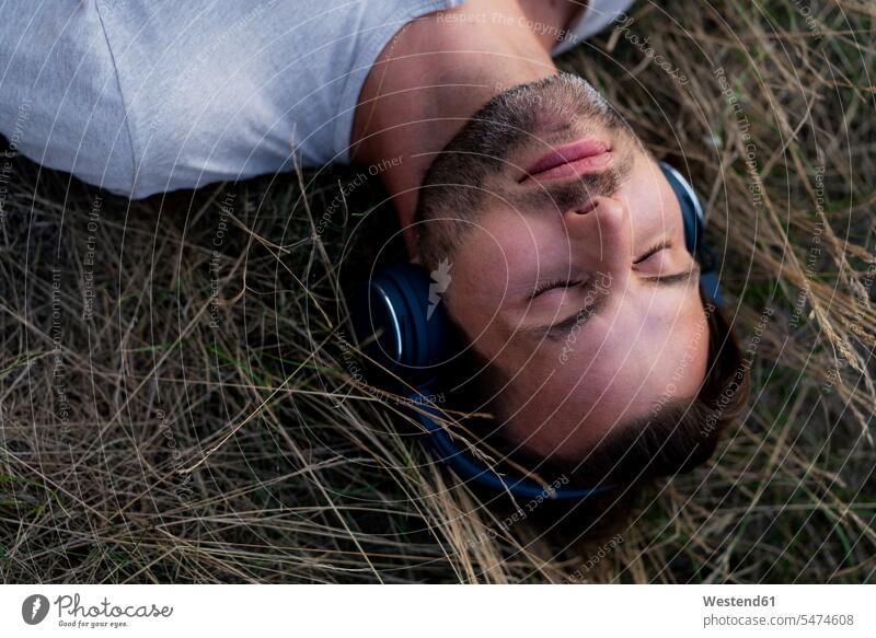 Relaxed man lying in field listening to music with headphones headset Field Fields farmland men males laying down lie lying down relaxed relaxation hearing