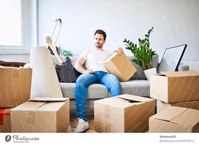 Frustrated man sitting on couch surrounded by cardboard boxes Frustration frustrating packing case packing cases Seated settee sofa sofas couches settees men