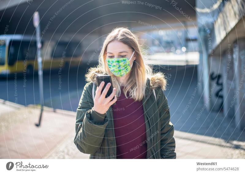 Young woman with smartphone wearing mask in the city coat coats jackets transport motor vehicles road vehicle road vehicles buses busses telecommunication