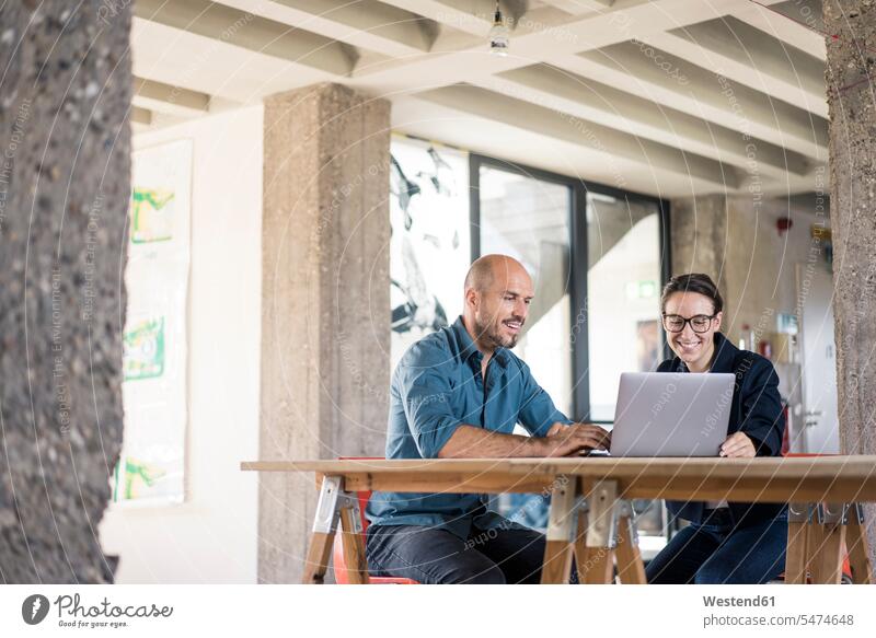 Smiling businessman and woman using laptop while working at office color image colour image indoors indoor shot indoor shots interior interior view Interiors