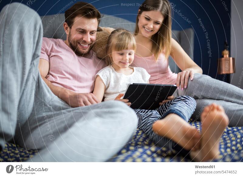 happy family sitting on bed, watching something on digital tablet with little daughter families beds daughters happiness Seated digitizer Tablet Computer