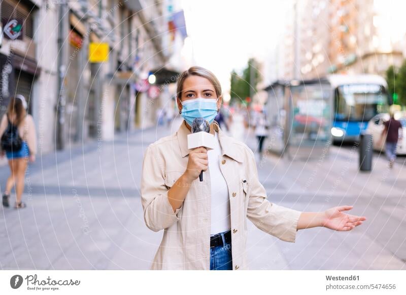Female reporter wearing mask talking over microphone on street in city color image colour image Spain outdoors location shots outdoor shot outdoor shots day