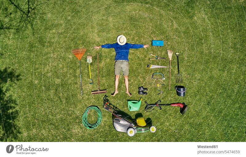 View from above of a gardener with sun hat on his face, laying on the grass with all the tools he need for take care of garden gardeners buckets brooms shoes