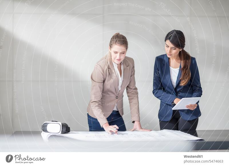 Two young women with tablet and VR glasses working on blueprint in office At Work Table Tables specs Eye Glasses spectacles Eyeglasses Office Offices woman