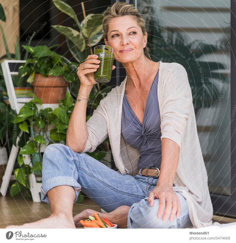 Portrait of smiling mature woman sitting at open terrace door drinking green smoothie Crockery Tableware Drinking Glass Drinking Glasses Bowls relax relaxing
