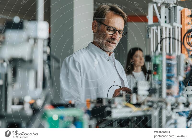 Mature man examining machinery with female colleague in background at laboratory color image colour image indoors indoor shot indoor shots interior