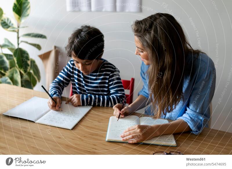 Young woman sitting with student doing homework on table at home color image colour image Spain casual clothing casual wear leisure wear casual clothes