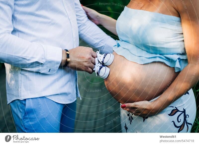 Man touching belly of pregnant woman with baby booties color image colour image outdoors location shots outdoor shot outdoor shots day daylight shot