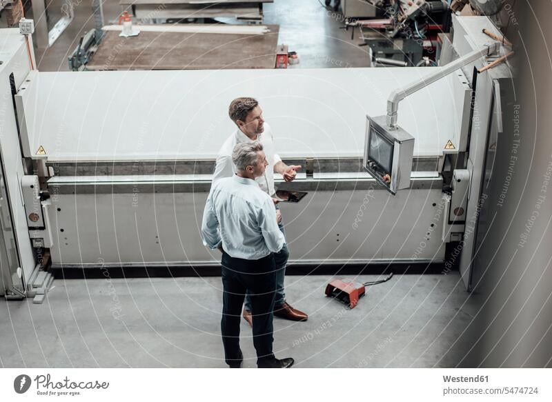 Mature male engineers discussing over manufacturing equipment in factory color image colour image Germany indoors indoor shot indoor shots interior
