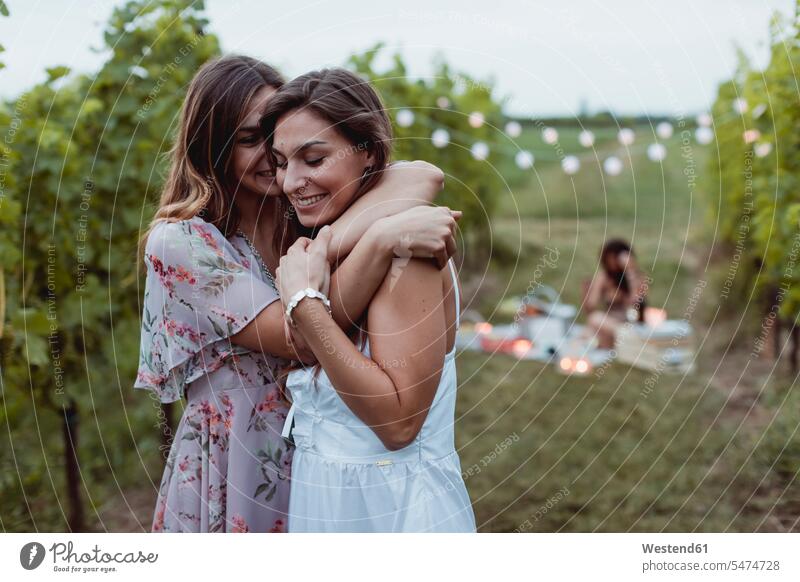 Twin sisters embracing at summer picnic in a vineyard embrace Embracement hug hugging female friends tipsy Picnic picnicking mate friendship Food foods