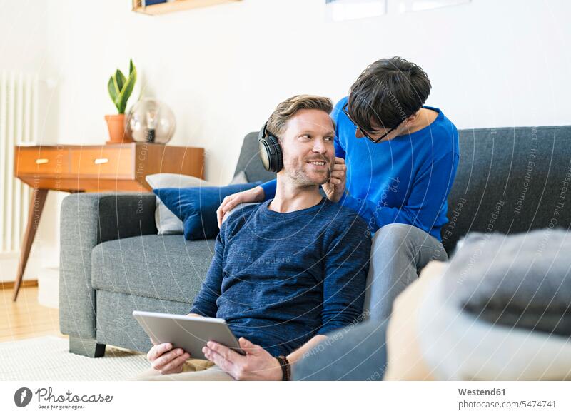 Casual couple with headphones relaxing on lounge couch in their modern living room settee sofa sofas couches settees tablet digitizer Tablet Computer Tablet PC