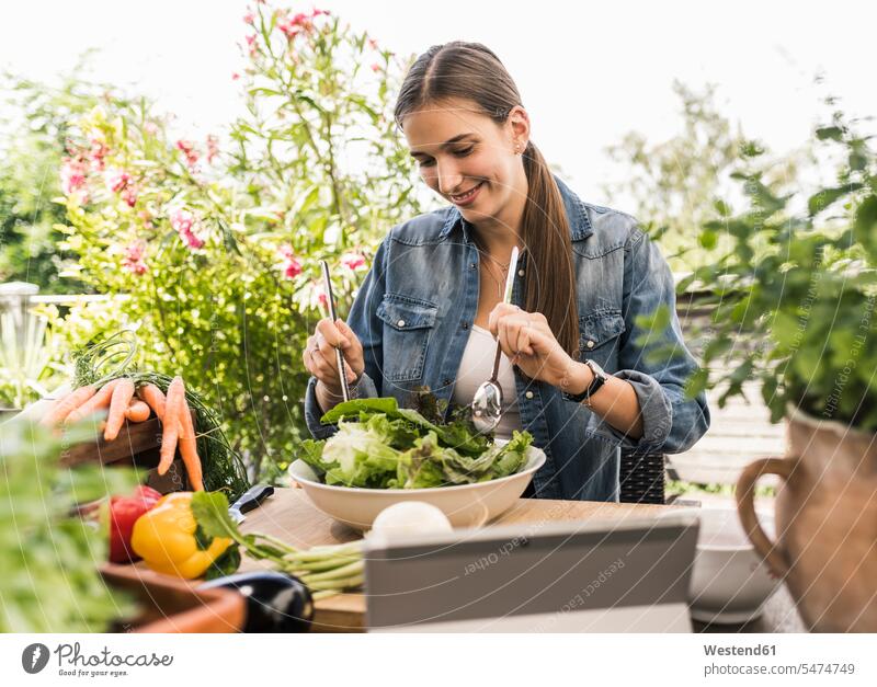 Smiling young woman preparing salad on table in yard color image colour image Germany leisure activity leisure activities free time leisure time casual clothing