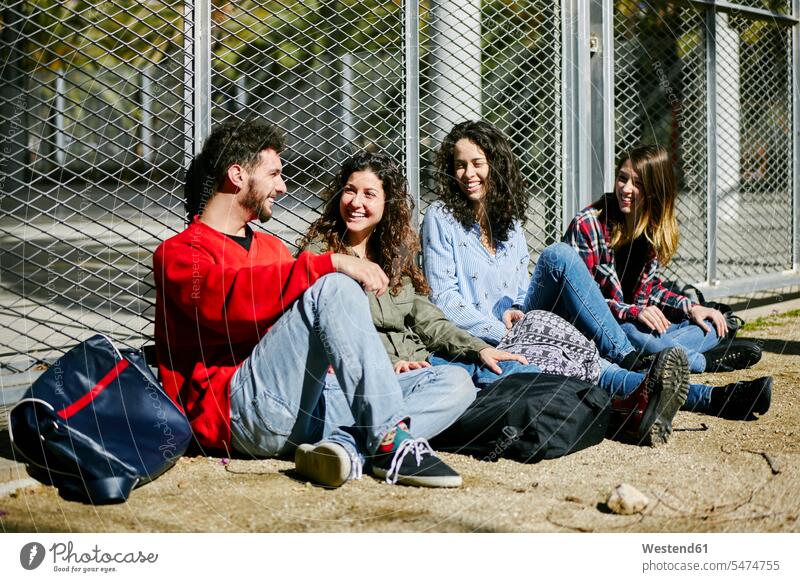 Four happy friends sitting at fence talking Seated happiness group of people Group groups of people speaking persons human being humans human beings friendship