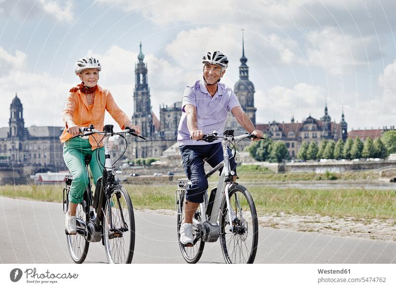 Smiling senior couple riding electric bicycle while exploring Hausmannsturm, Dresden, Germany color image colour image outdoors location shots outdoor shot