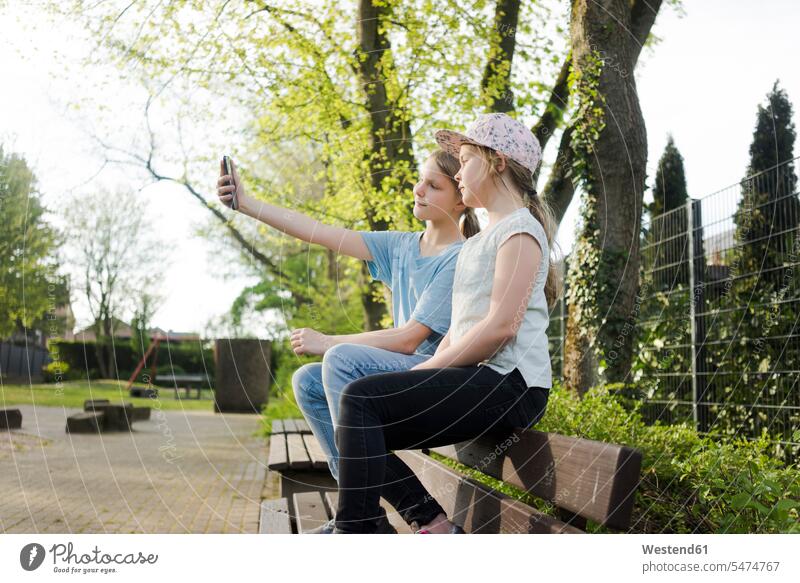 Two girls sitting on a park bench taking a selfie human human being human beings humans person persons caucasian appearance caucasian ethnicity european 2