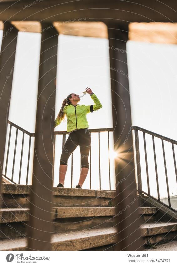 Sportive young woman standing on stairs drinking from bottle sportive sporting sporty athletic Bottle Bottles females women stairway sports Adults grown-ups