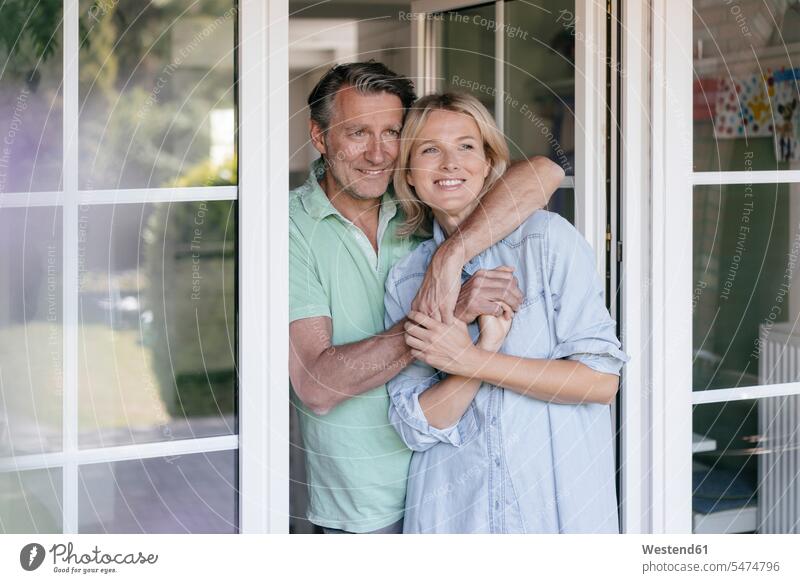 Happy mature couple hugging at French window happiness happy embracing embrace Embracement twosomes partnership couples terrace door patio door people persons