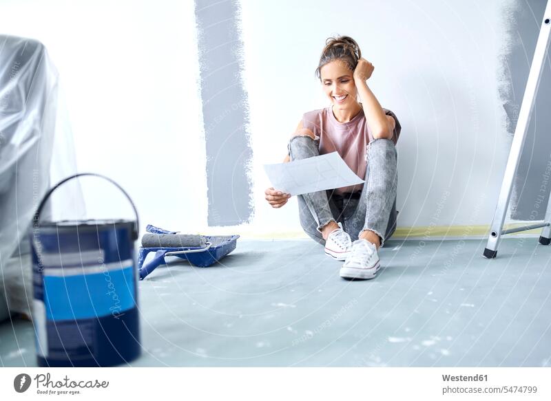 Smiling woman with head in hands holding paper while sitting on floor at home color image colour image indoors indoor shot indoor shots interior interior view