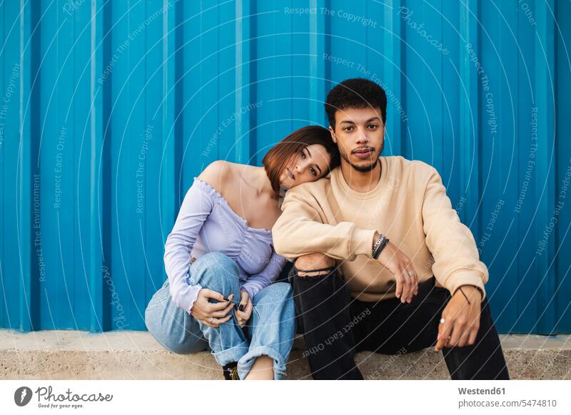 Girlfriend leaning on boyfriend's shoulder while sitting against blue wall color image colour image outdoors location shots outdoor shot outdoor shots day