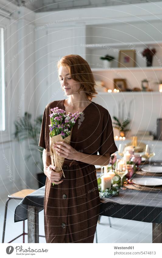 Redheaded woman holding bunch of flowers, standing in front of laid table shelf Shelve rack racks shelves three-quarter length three quarter length Preparation