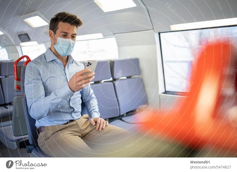 Businessman wearing protective face mask using mobile phone while sitting in train color image colour image Vehicle Interior day daylight shot daylight shots