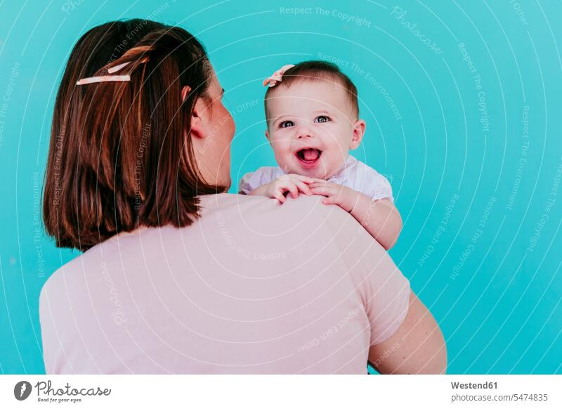 Mother and baby girl in front of turquoise wall smile big smile laughing open smile human human being human beings humans person persons 2 2 people 2 persons