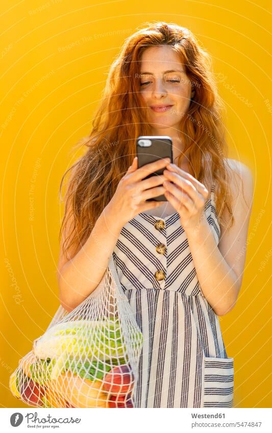 Smiling young woman using smart phone while standing against yellow background color image colour image Spain leisure activity leisure activities free time