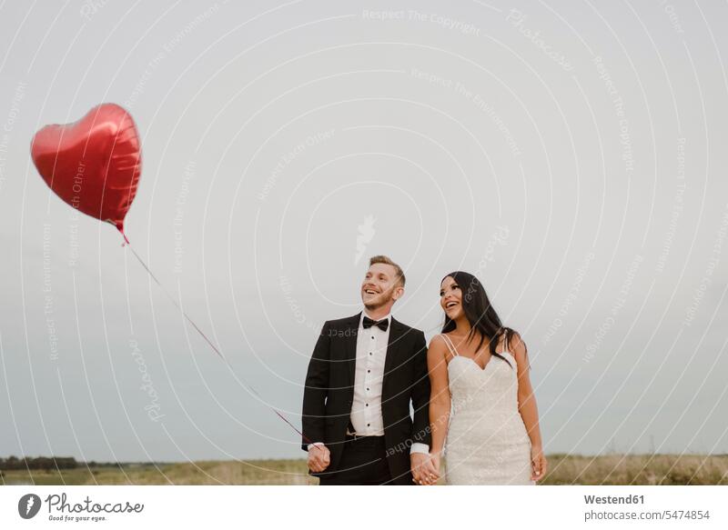 Happy bride and groom with heart shape balloon against sky color image colour image outdoors location shots outdoor shot outdoor shots day daylight shot