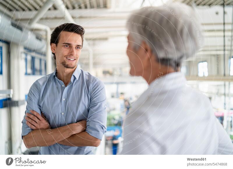 Smiling businessman talking to senior businesswoman in a factory smiling smile factories Businessman Business man Businessmen Business men businesswomen