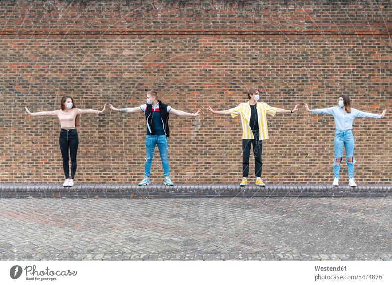 Male and female friends with arms outstretched maintaining safe distance while standing against brick wall color image colour image outdoors location shots