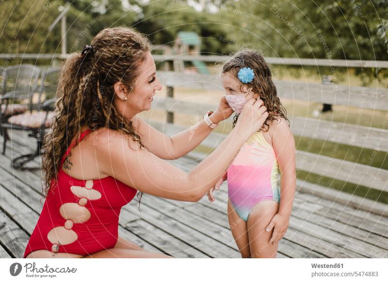 Mother in swimsuit applying protective face mask on daughter human human being human beings humans person persons caucasian appearance caucasian ethnicity