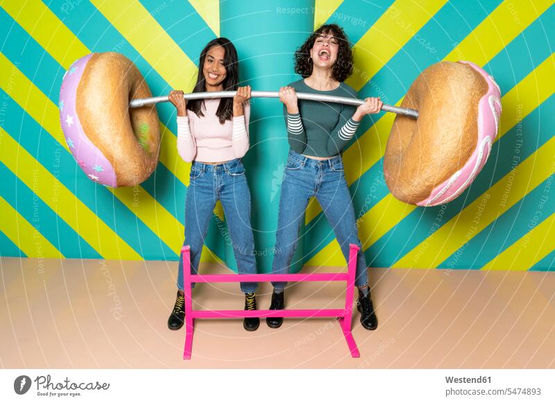 Two happy young women at an indoor theme park having fun with oversized donuts Spain doughnut Doughnuts playful toothy smile big smile open smile laughing