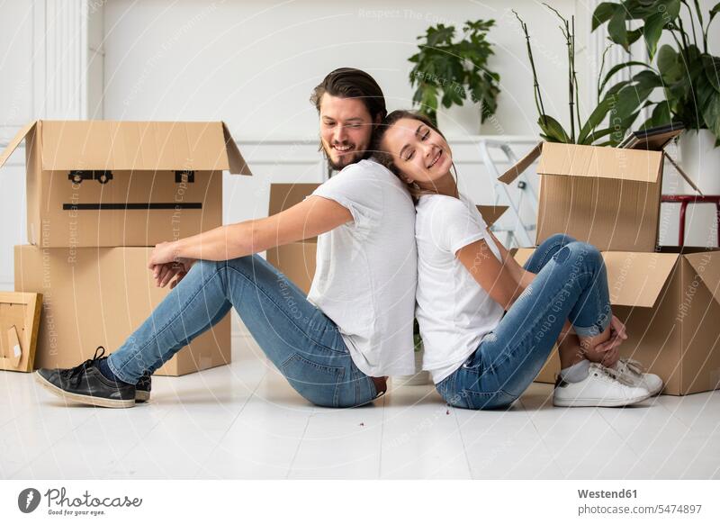 Happy couple with cardboard boxes sitting on the floor in new home smiling smile at home moving house move Moving Home Cardboard Carton carton Cardboards