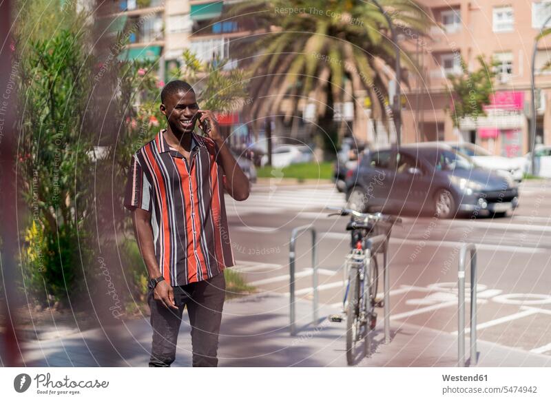 Smiling young man talking on smart phone while standing on footpath in city color image colour image day daylight shot daylight shots day shots daytime Spain