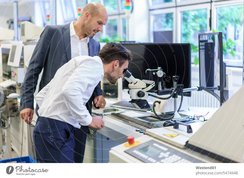 Young engineer looking through microscope while standing by businessman at laboratory color image colour image indoors indoor shot indoor shots interior