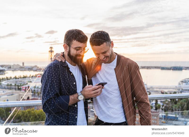 Gay couple using cell phone on lookout above the city with view to the port, Barcelona, Spain associate associates partner partners partnerships touristic