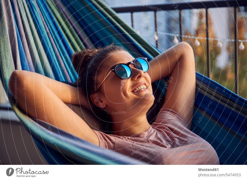 Portrait of happy young woman with sunglasses lying on hammock on balcony human human being human beings humans person persons caucasian appearance