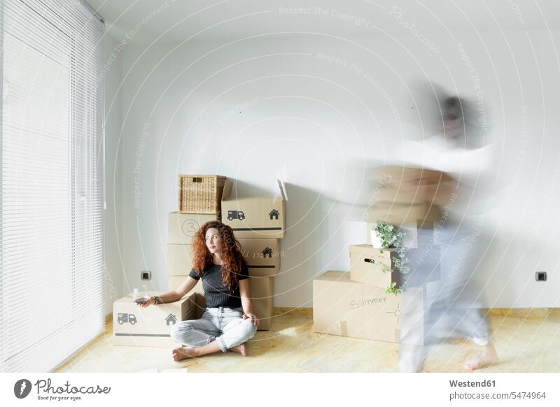 Young woman sitting in new home with glass of red wine while friend is moving fast with cardboard box friends mate female friend human human being human beings